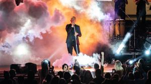 A man performs on stage with smoke and a light show